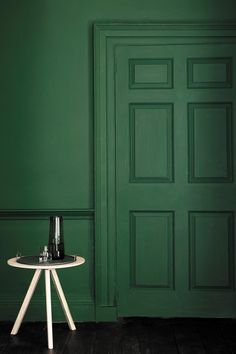 a small table with two bottles on it in front of a green wall and door