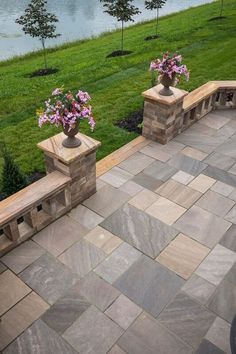 two vases filled with flowers sitting on top of a stone wall next to a lake