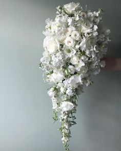 a bouquet of white flowers is held up by someone's hand against a gray wall