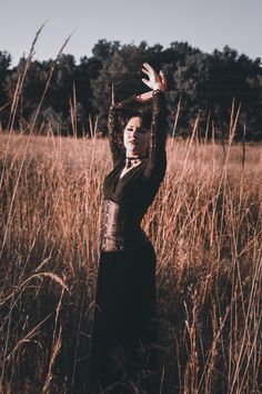 a woman standing in tall grass holding her hands up