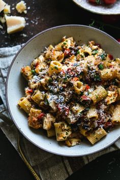 a white bowl filled with pasta and meat on top of a table next to cheese