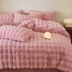 a bed with pink comforter and pillows on it in a bedroom next to a night stand