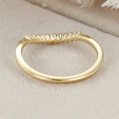 a yellow gold wedding band with leaves on it, sitting on a white clothed surface