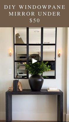 a black vase sitting on top of a wooden table next to a wall mounted mirror