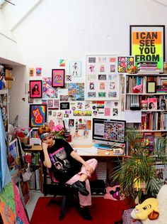 a woman sitting on a chair in front of a desk filled with books and pictures