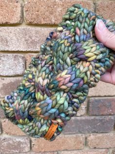 a hand is holding up a multicolored knitted object in front of a brick wall