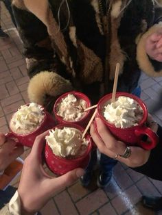 four people holding red mugs filled with whipped cream