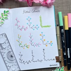 an open notebook with flowers and rulers on it next to markers, pencils and pens