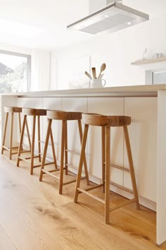 three wooden stools sitting in front of a kitchen island with white counter tops and cabinets