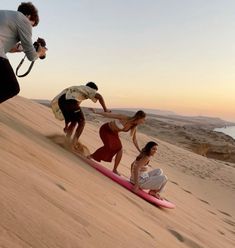 three people standing on top of a sand dune next to a surfboard and camera