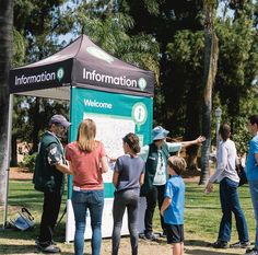 a group of people standing in front of a information sign at a park with palm trees