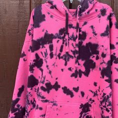 a pink and black tie dye hoodie hanging on a wooden wall