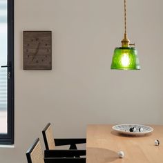 a green light hanging over a wooden table in front of a clock on the wall