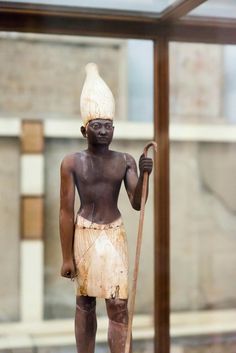 a statue of a man holding a stick and wearing a white headdress, standing in front of a glass window