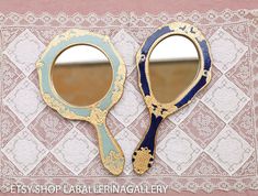 two blue and gold mirrors sitting on top of a lace covered table cloth next to each other