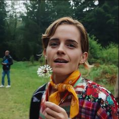 a woman holding a flower in her hand and wearing a yellow scarf around her neck