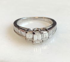 Here is a beautiful 14k white gold emerald cut diamond ring. The center stone is .20ct. with 2 side emerald cut diamonds totaling .30ct. There are also 16 baguettes in the band totaling .56ct. A beauty that will get a lot of compliments! Metal: 14K White Gold Diamonds: 1-Emerald Cut .20cttw, 2-Emerald cut .30cttw, G/H, VS, 16-side stones .56cttw, Weight: 3.8 grans Size: 6.5 SKU# 21SB080619 If you have any questions on this item, please message us! GandDJewelers.etsy.com Please note that all of o Fine Jewelry Emerald Cut Diamond Ring With Baguette Diamonds, White Emerald Cut Platinum Diamond Ring, Classic Emerald Cut Baguette Diamond Wedding Ring, Octagon White Gold Diamond Ring With Baguette Diamonds, White Gold Octagon Diamond Ring With Baguettes, White Gold Octagon Diamond Ring With Baguette Diamonds, Classic Emerald Cut Baguette Diamond Ring, Platinum Diamond Ring With Baguette Emerald Cut, White Emerald Cut Platinum Emerald Ring