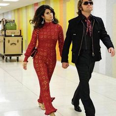 a man and woman are walking down the hall together in red outfits, with luggage behind them