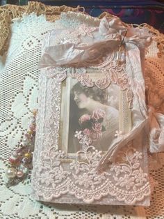 an old photo frame is sitting on a lace doily with pink flowers in it