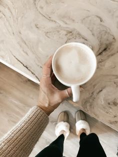 a person holding a cup of coffee in their hand while standing on the floor next to a marble wall