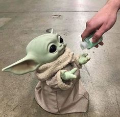 a baby yoda doll is being fed by someone's hand while they are on the floor