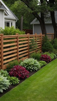 a wooden fence in front of a house with flowers growing on the side and green grass around it