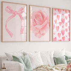 three pink roses are hanging on the wall above a white couch with pillows and blankets