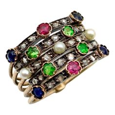 This is part of Chairish’s Fine Jewelry assortment.  This beautiful 14k gold Edwardian harem ring contains an array of Rose Cut diamonds, pearls, sapphires, rubies, and green demantoid garnets. The ring consists of five 14k gold bands, held together at the bottom in a half-hoop that connects the bands and makes them easy to wear. What is most alluring about the ring is the stacked effect of the gemstones interspersed in a layered pattern. The stones are bezel set in a tulip bezel, with the excep Antique Green Multi-stone Ring, Harem Rings, Dramatic Necklace, Demantoid Garnet, Diamond Dangle Earrings, Ruby Sapphire, Emerald Cut Diamonds, Contemporary Jewelry, Rose Cut Diamond