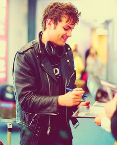 a man in a black leather jacket is looking at his cell phone while standing next to another person