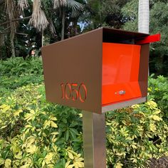 an orange mailbox sitting in the middle of some bushes