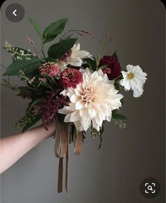 a bouquet of flowers is being held up by someone's hand on a gray background