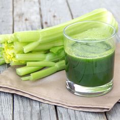 a glass filled with green liquid next to celery on top of a napkin