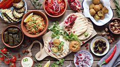 an assortment of food is laid out on a wooden table, including pita breads and olives