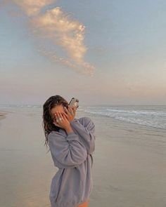 a woman is standing on the beach talking on her cell phone and looking at something