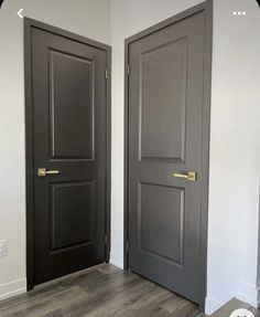 two black doors in the corner of a room with white walls and wood flooring