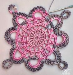 a crocheted doily with pink and gray circles on it, next to a knitting needle