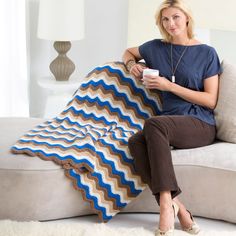 a woman sitting on a couch holding a coffee cup and a crocheted blanket