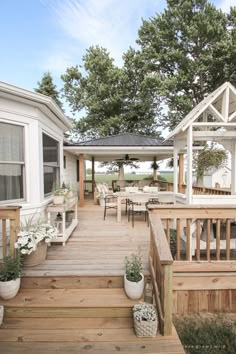 a wooden deck with potted plants and chairs on it next to a white house