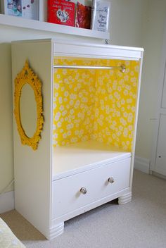 a white dresser with yellow flowers on it and a mirror mounted to the wall next to it