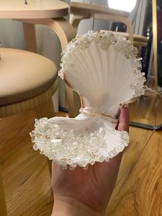 a hand holding an open shell on top of a wooden table next to a chair