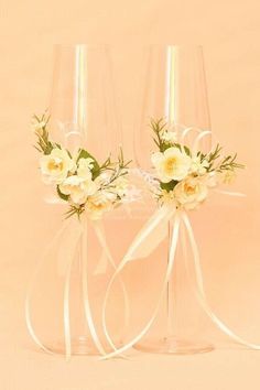 two wine glasses with flowers in them on a pink background, one has a white ribbon and the other is clear