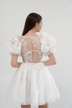 the back of a woman wearing a white dress with sheer lace and flowers on it