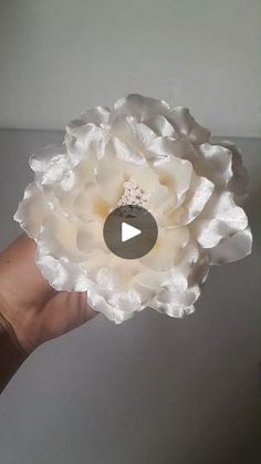 a hand holding a white flower with a video in it's center and the words, how to make paper flowers