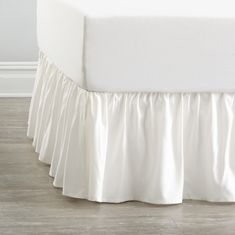 a white bed with ruffled bedskirt on the top and bottom edge, in front of a wall