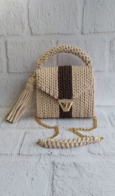 a white purse with a brown and tan stripe on the front, sitting against a brick wall