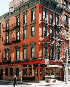 an old brick building on the corner of a street with fire escape stairs and people walking by