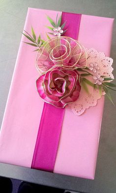 a pink gift wrapped in lace and ribbon with a flower on the top is sitting on a table