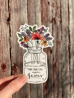 a hand holding up a sticker with flowers in a mason jar