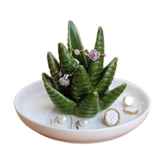 a white plate with some green plants on it and other jewelry items in the bowl