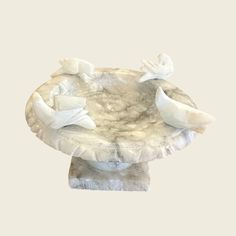 a white marble bowl with two birds on it's side and one bird sitting on the base